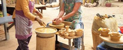 A Cambodian woman teaches a senior volunteer traditional Khmer pottery. An older volunteer participates in a pottery class as part of her Khmer cultural experience in Cambodia.